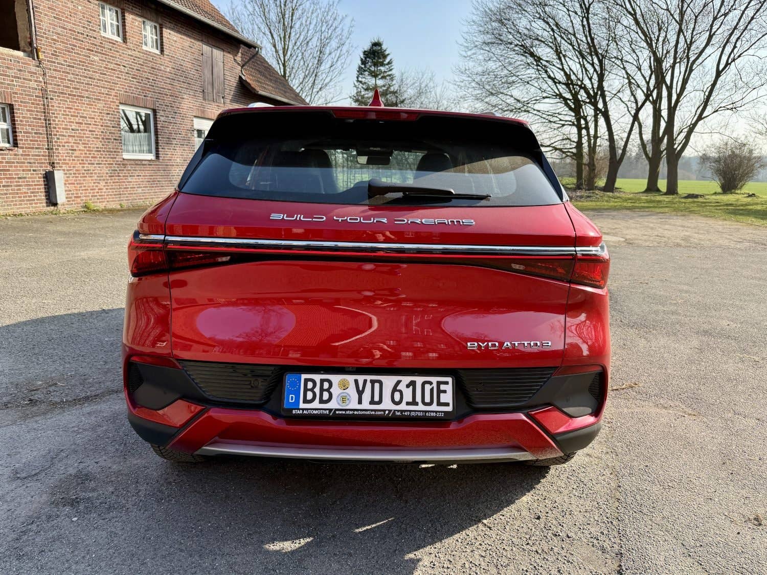 Véhicule électrique BYD Atto 3 rouge garé, montrant l'arrière avec 'BUILD YOUR DREAMS' sur le coffre.