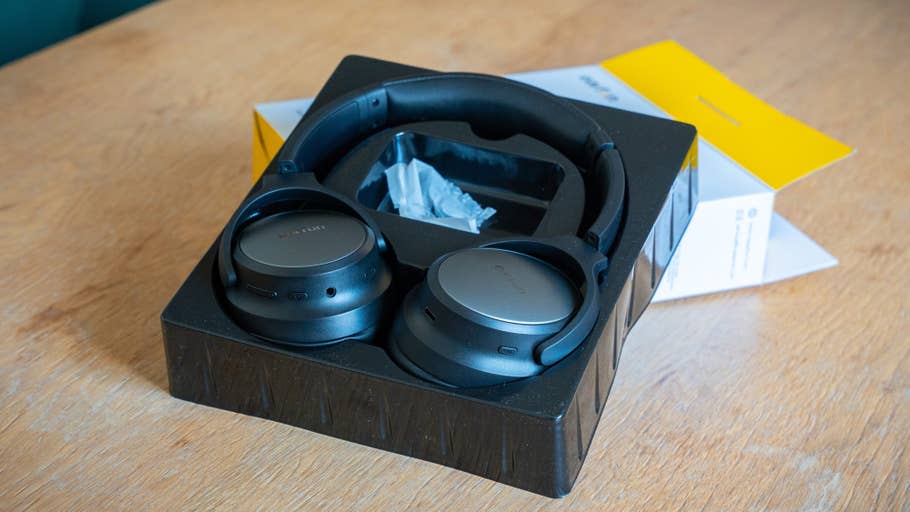 Casque audio noir supra-auriculaire dans un emballage sur une table en bois.