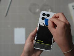 Une personne utilise un outil pour ouvrir l'arrière d'un smartphone Fairphone 6, révélant la batterie à l'intérieur.