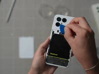 Une personne utilise un outil pour ouvrir l'arrière d'un smartphone Fairphone 6, révélant la batterie à l'intérieur.