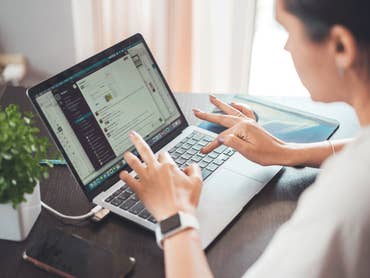 Une femme tape sur un ordinateur portable avec une petite plante et un smartphone sur la table.