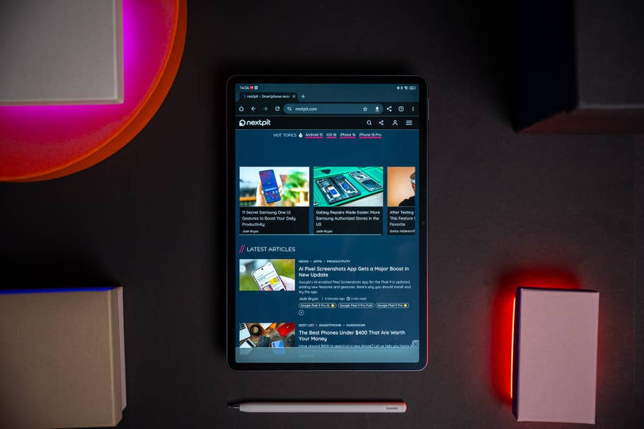 Une Huawei MatePad Air affichant un site Web avec des articles et un stylet, entourée de lumières colorées et de boîtes.