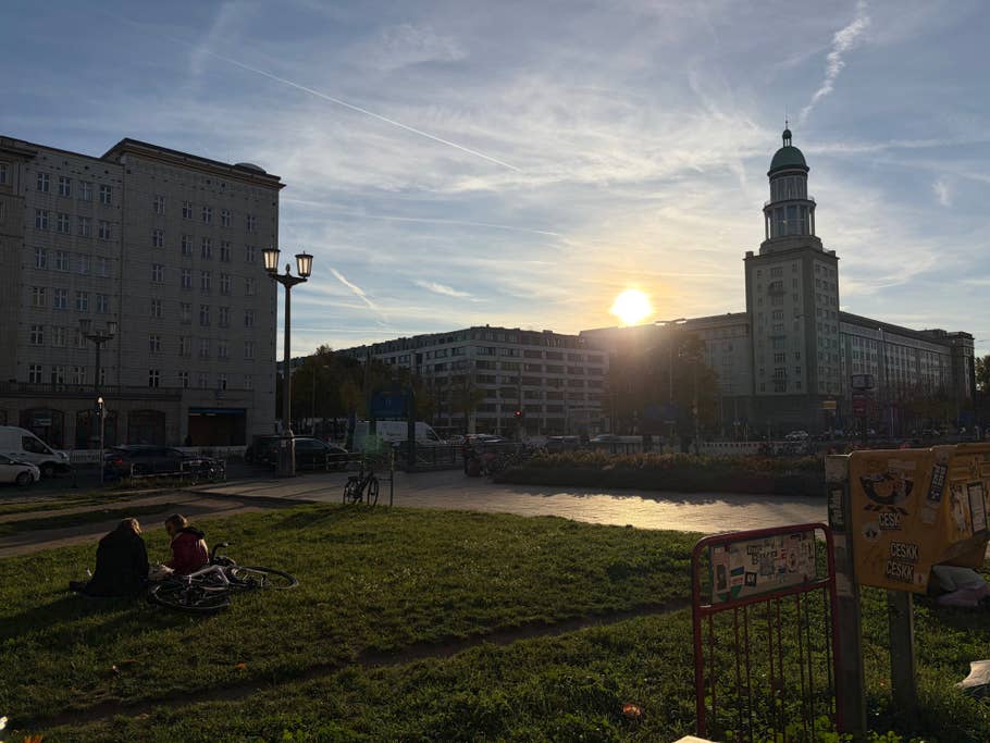 Coucher de soleil sur un paysage urbain avec des gens assis sur l'herbe, des vélos à proximité.
