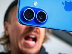 Gros plan d'une caméra bleue d'Apple iPhone 16 avec une personne criant en arrière-plan.