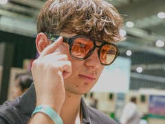 Un jeune homme portant des lunettes de soleil élégantes, se touchant la tempe, dans un espace intérieur.