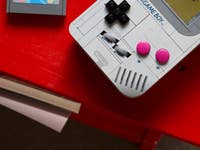 Une réplique LEGO d'une Game Boy sur une table rouge avec une cartouche de jeu à côté.