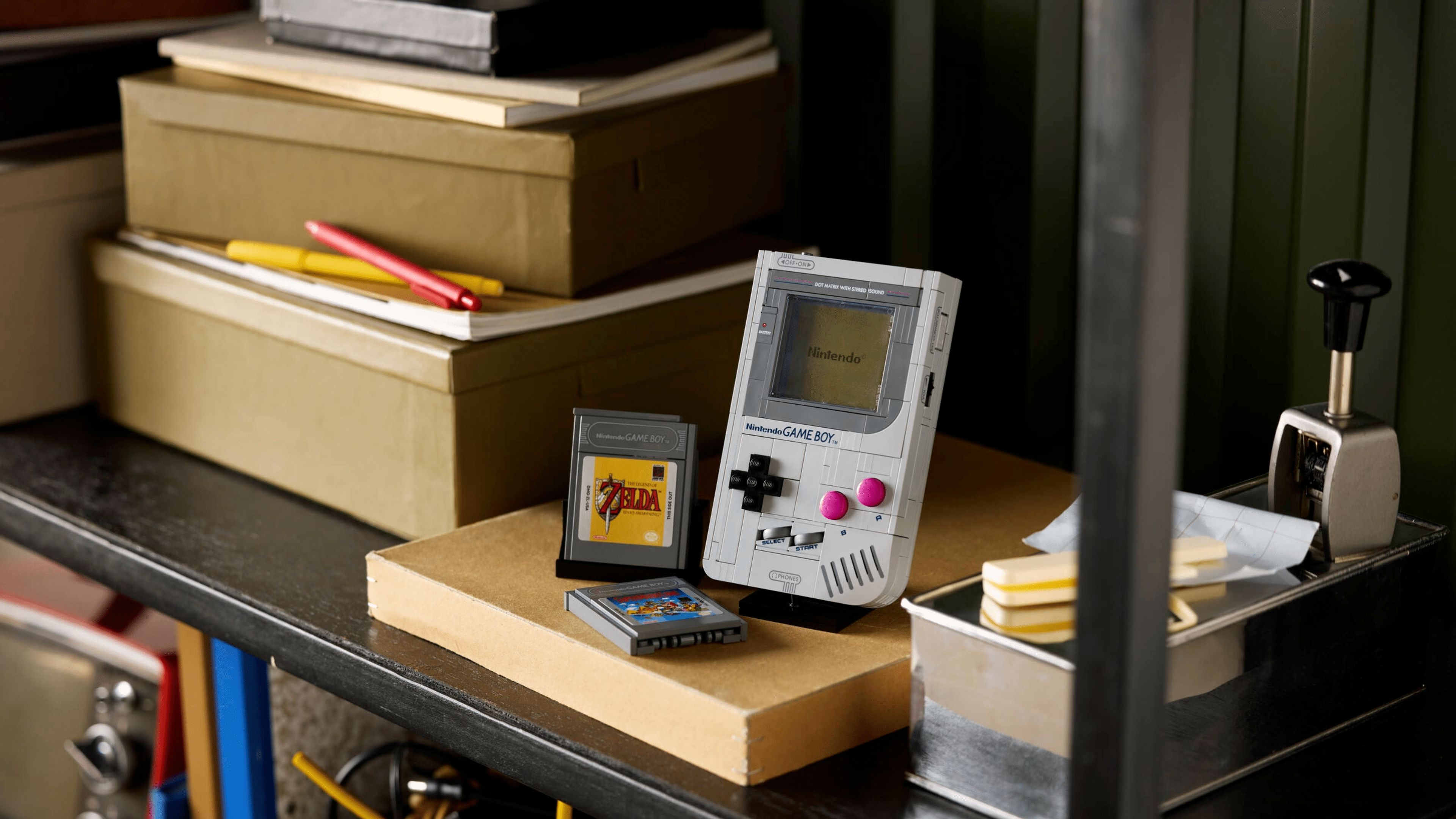 Un Game Boy vintage avec des cartouches de jeu sur une étagère encombrée parmi des boîtes et des fournitures de bureau.
