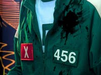 Une personne portant un survêtement vert avec le numéro 456 et un badge rouge 'X', taché d'éclaboussures.