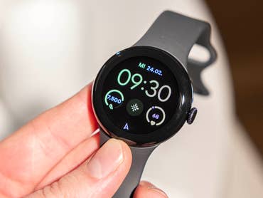 La Google Pixel Watch 2 vue de face et de haut tenue dans une main gauche avec son écran allumé