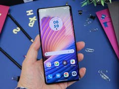 Le Motorola Edge 40 Pro vu de face et de haut, tenu dans une main gauche avec son écran allumé et avec un fond bleu et violet en arrière-plan