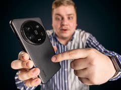 Un homme vu de haut tenant un Xiaomi 14 Ultra dans sa main droite et touchant le dos du smartphone avec son index gauche