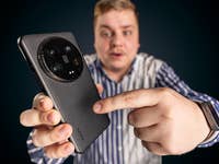 Un homme vu de haut tenant un Xiaomi 14 Ultra dans sa main droite et touchant le dos du smartphone avec son index gauche