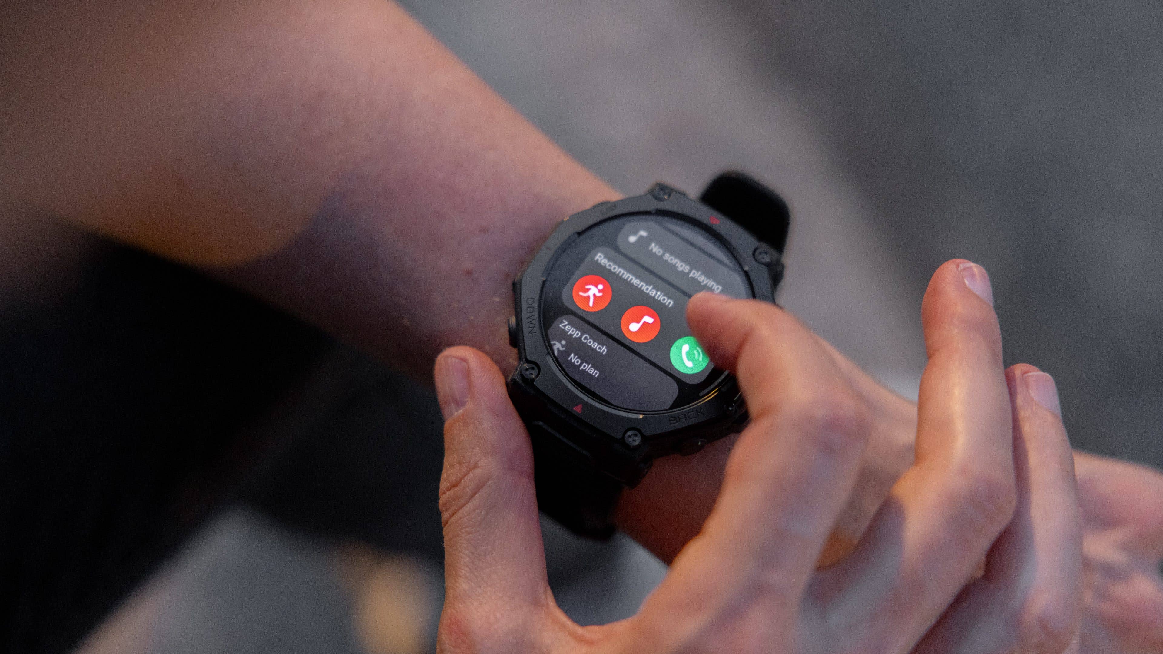 Une personne utilisant une montre connectée Amazfit T-Rex Pro 3 affichant des options pour la musique et le coaching.