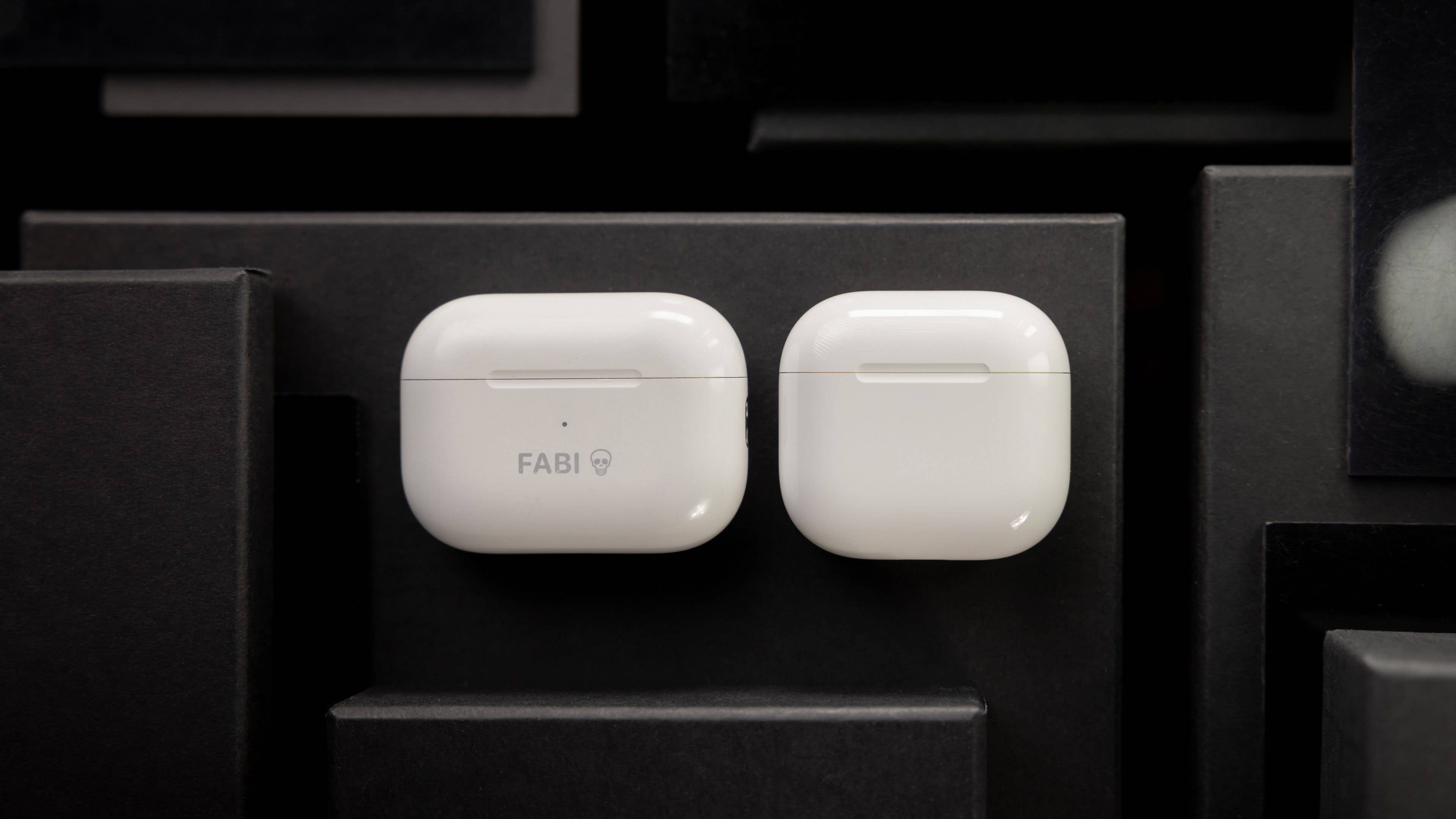 Coques AirPods blanches d'Apple sur fond sombre, l'une avec le texte 'FABI'.