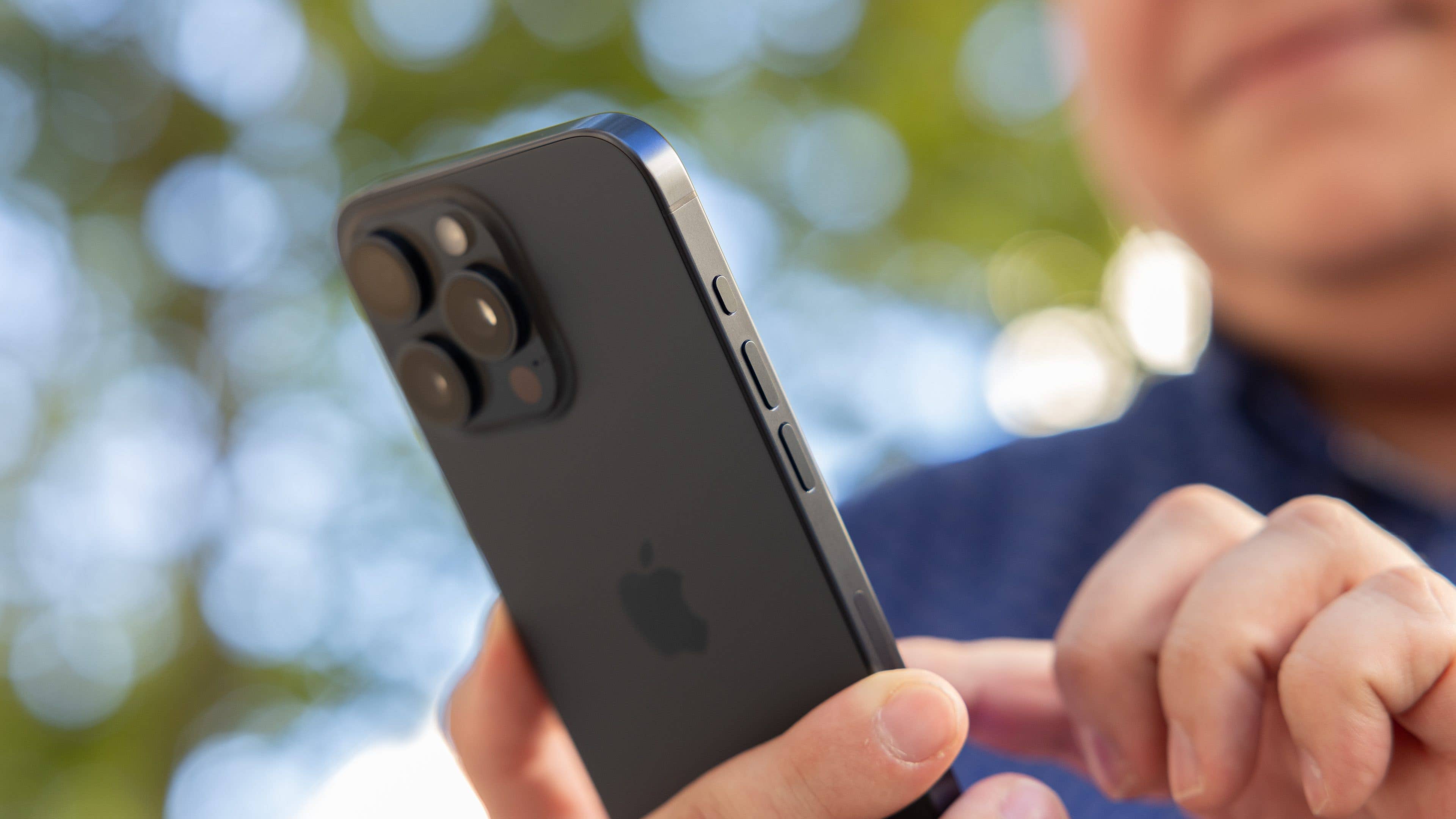 L'iPhone 15 Pro Max d'Apple vu de dos en plein soleil tenu dans une main droite