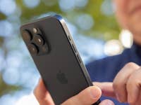 L'iPhone 15 Pro Max d'Apple vu de dos en plein soleil tenu dans une main droite