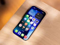 Un iPhone avec une mise en page d'application colorée sur une surface en bois, affichant des widgets météo et calendrier.