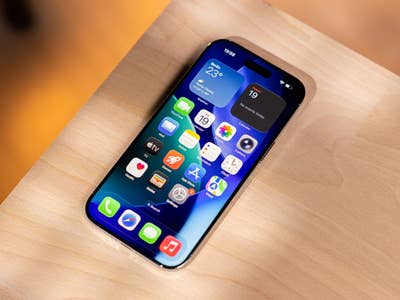 Un iPhone avec une mise en page d'application colorée sur une surface en bois, affichant des widgets météo et calendrier.