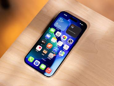 Un iPhone avec une mise en page d'application colorée sur une surface en bois, affichant des widgets météo et calendrier.