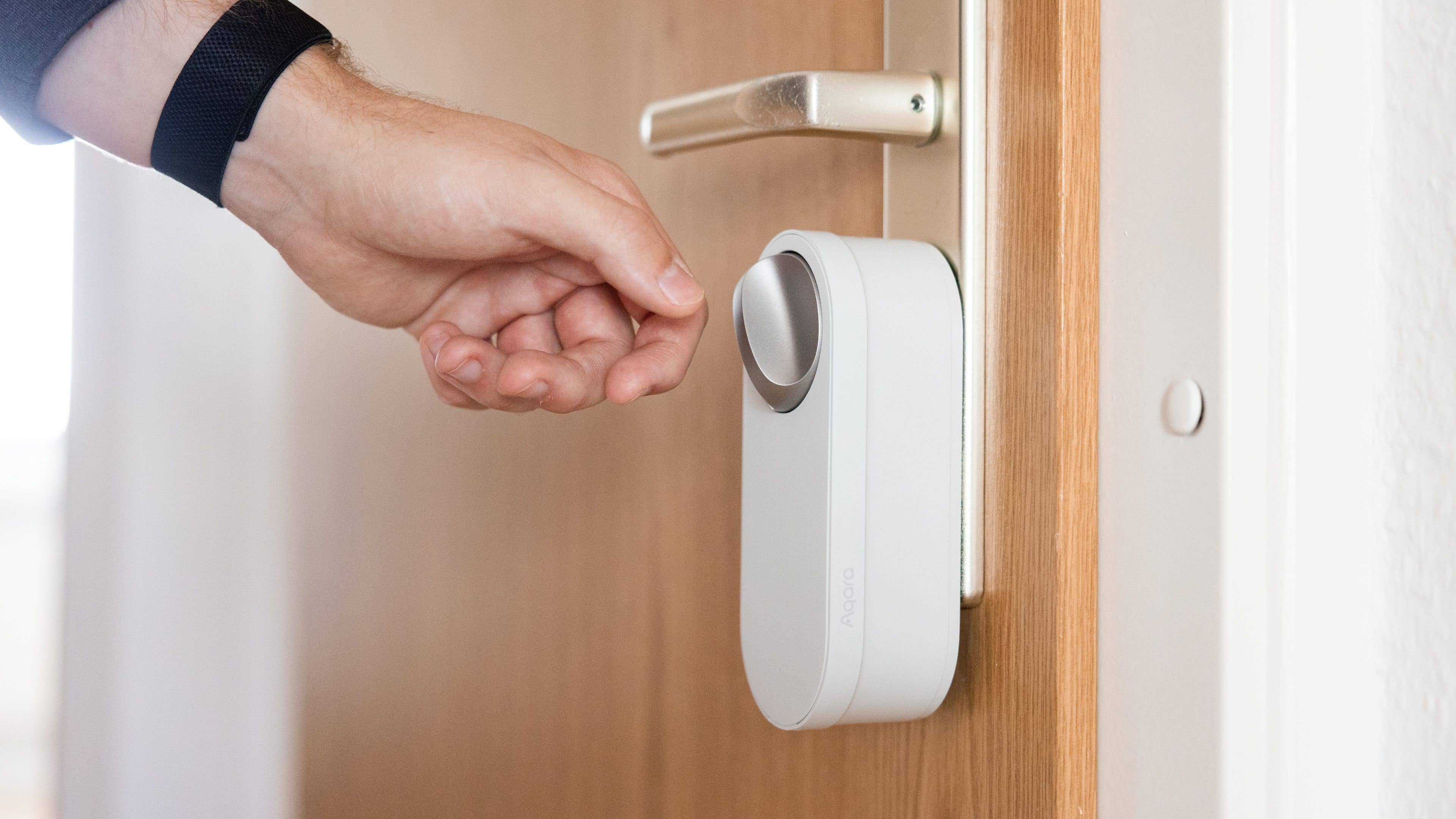 nextpit_Aqara_U200_Lite_Test_1.jpg Une main atteignant une serrure de porte intelligente installée sur une porte en bois.