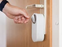Une main atteignant une serrure de porte intelligente installée sur une porte en bois.