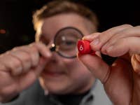 Un homme vu de face tenant un écouteur rouge dans sa main gauche et une loupe dans sa main droite, orientée vers l'écouteur.