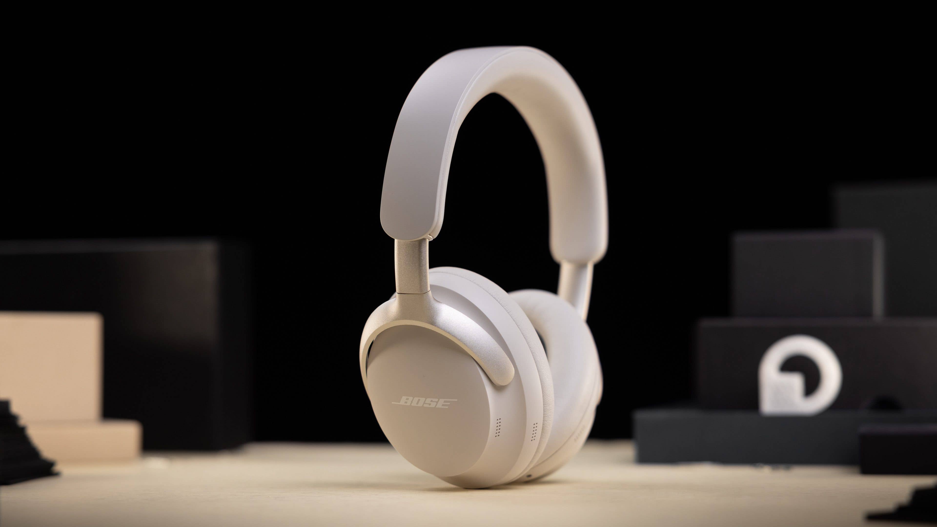 Le Bose QC Ultra Headphones vu de côté et posé verticalement sur une table en bois avec un arrière-plan noir