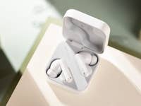 Écouteurs sans fil blancs dans leur étui de chargement sur une surface claire.