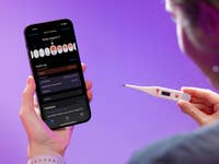 Une personne tenant un test de grossesse dans une main et un smartphone avec une application de santé dans l'autre