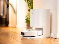 Un aspirateur robot blanc amarré à un mur avec des plantes dans un espace intérieur moderne.