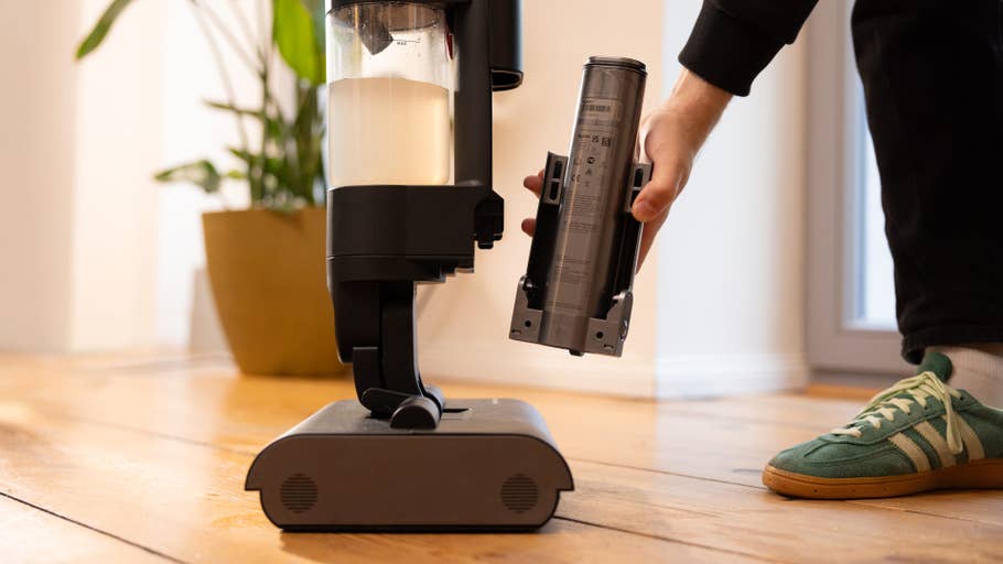 Une personne retire un réservoir du0027un nettoyeur Dyson Wash G1 sur un sol en bois.