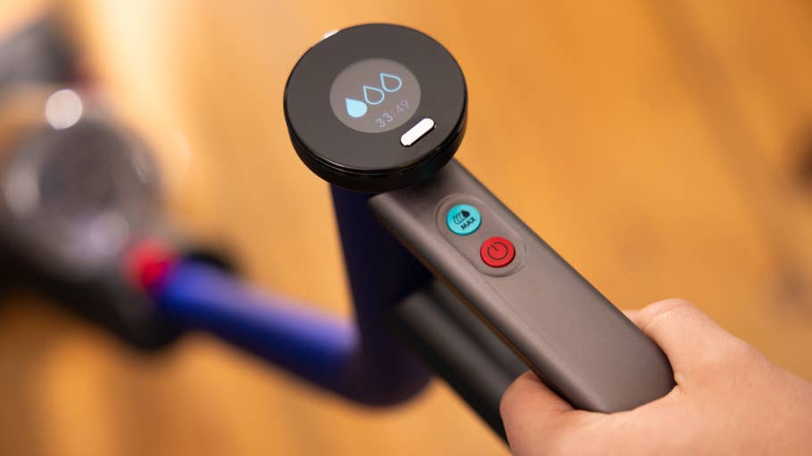 Gros plan du0027une poignée de dispositif de lavage Dyson affichant le niveau du0027eau et les commandes sur une surface en bois.