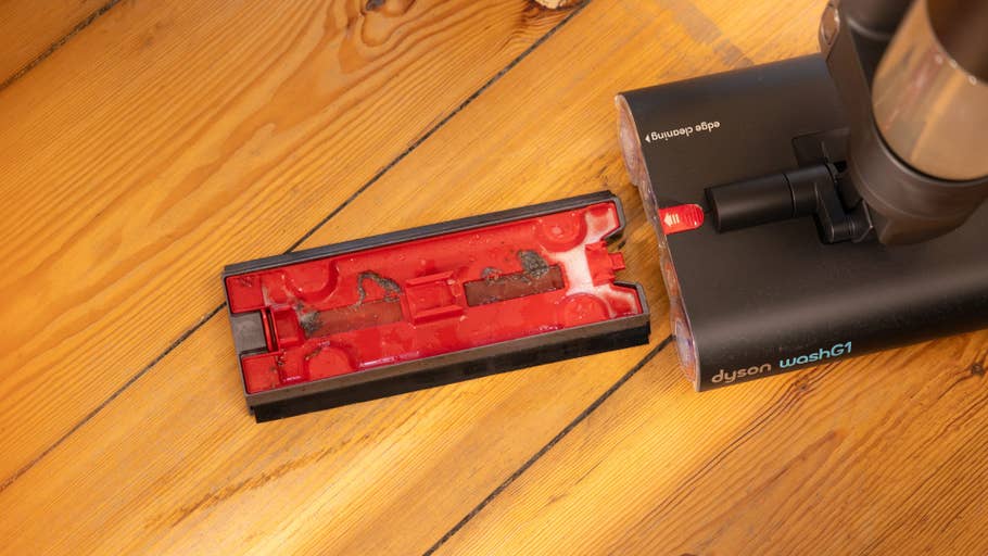 Aspirateur Dyson Wash G1 avec un accessoire de nettoyage détachable rouge et noir sur un sol en bois.