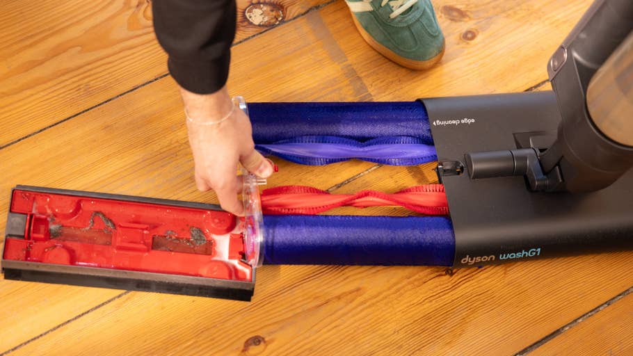 Une personne retire le conteneur de saleté du0027un aspirateur Dyson washG1 sur un sol en bois.