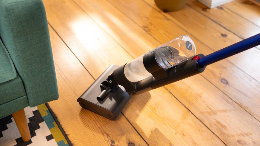 Un aspirateur Dyson Wash G1 nettoie un sol en bois près du0027un canapé vert.