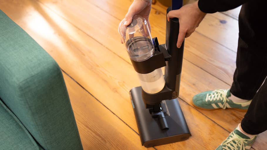 Une personne tient un aspirateur Dyson Wash G1 avec un réservoir à poussière transparent près du0027un canapé vert.