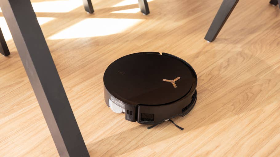 Un aspirateur robot Ecovacs Deebot X8 Pro Omni noir sur un sol en bois, placé sous une chaise.