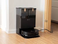 Un aspirateur robot Ecovacs Deebot X8 Pro Omni noir amarré à sa station de chargement dans une pièce.