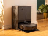 Un aspirateur robot Eufy X10 Pro Omni am doc à côté d'une plante dans une pièce ensoleillée.