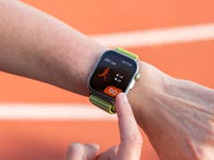 Une personne tient un smartphone affichant un plan d'entraînement 5K avec des indicateurs de performance sur une piste de course.