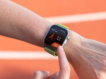 Une personne tient un smartphone affichant un plan d'entraînement 5K avec des indicateurs de performance sur une piste de course.
