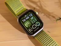 Huawei Watch Fit 4 Pro avec un bracelet vert affichant l'heure, la météo et des statistiques de fitness sur une surface en bois.