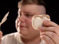 Un homme vu de face tenant dans une main les écouteurs Jabra Elite 10 Gen 2 et dans l'autre un câble audio jack.