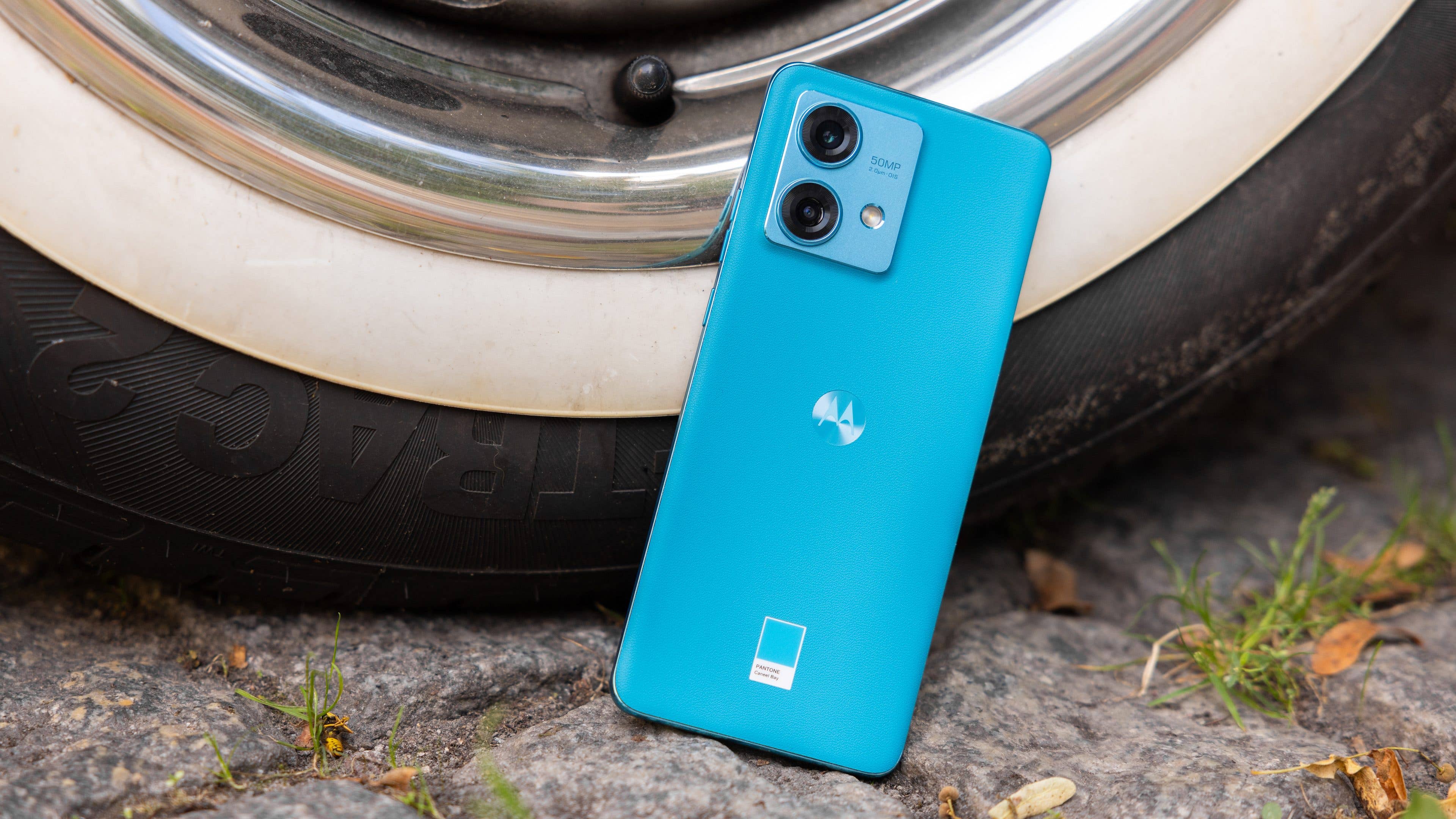 Le Motorola Edge 40 Neo vu de dos et posé par terre adossé contre une roue de voiture Le Motorola Edge 40 Neo vu de dos et posé par terre adossé contre une roue de voiture