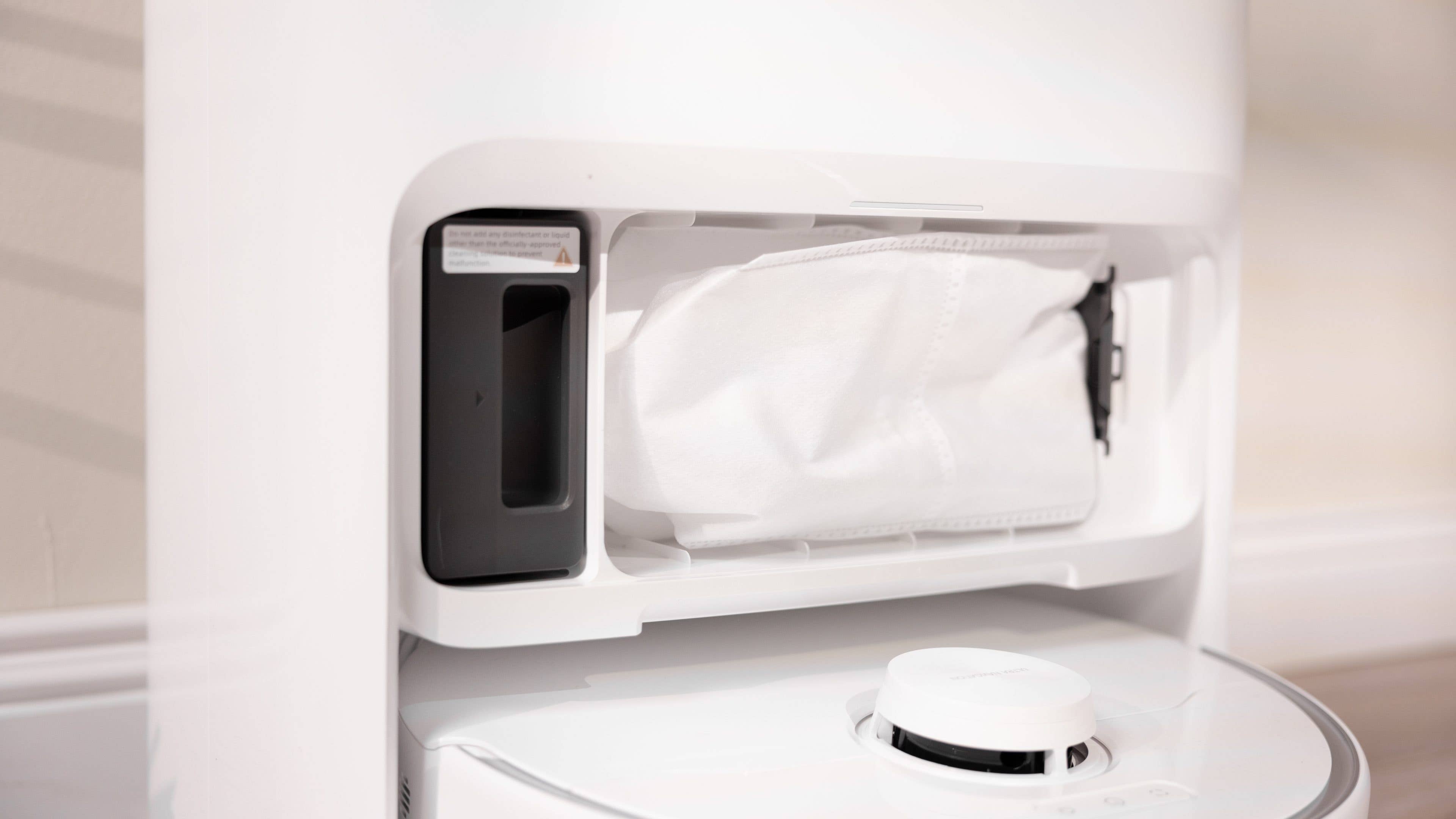 Gros plan du compartiment à poussière d'un aspirateur robot blanc montrant un sac à poussière amovible.