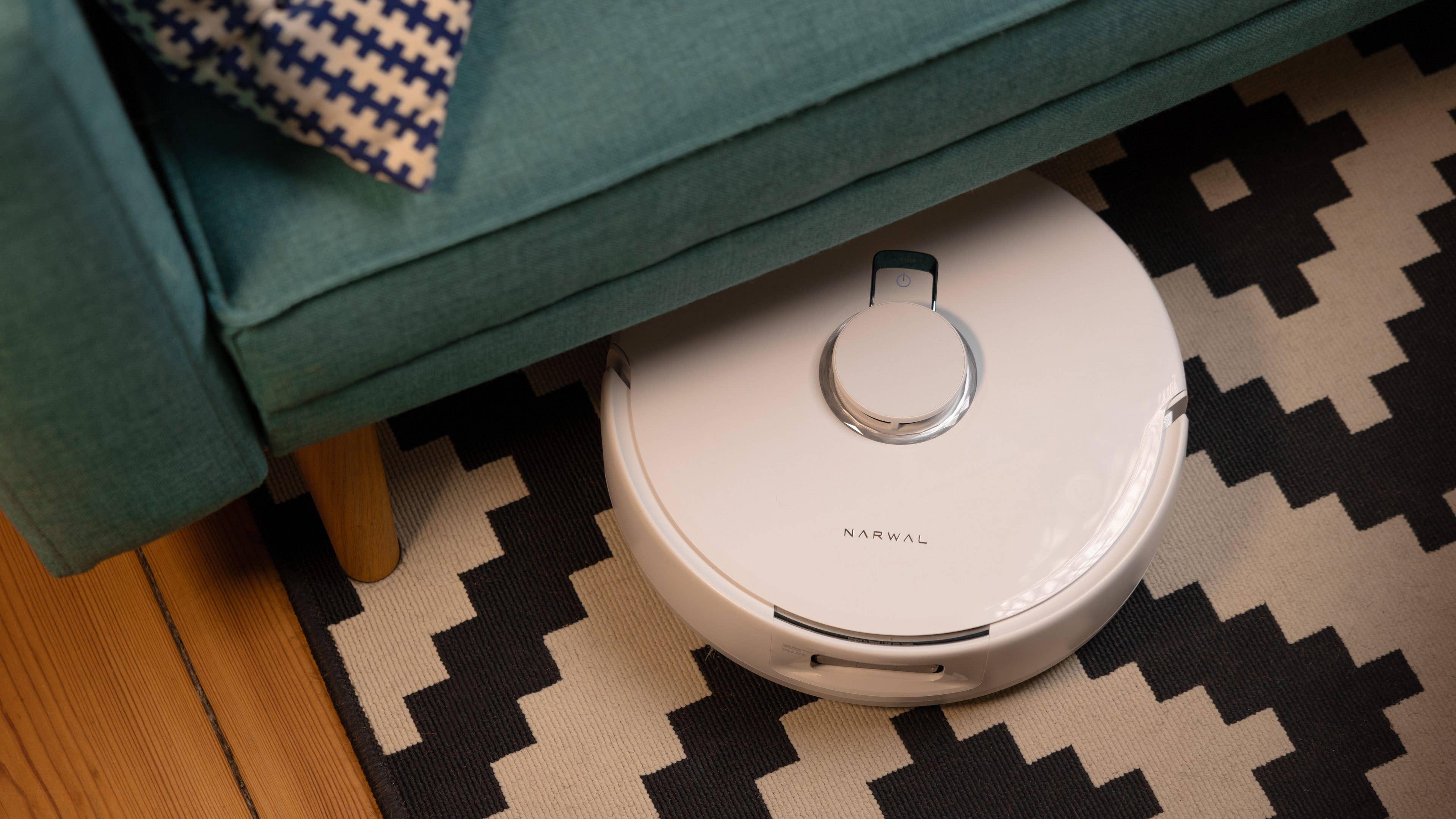 Le Narwal Freo X Ultra sur un tapis et caché en partie par un canapé