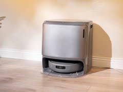 Un aspirateur robot gris élégant se trouve contre un mur dans une pièce bien éclairée.