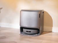 Un aspirateur robot gris élégant se trouve contre un mur dans une pièce bien éclairée.