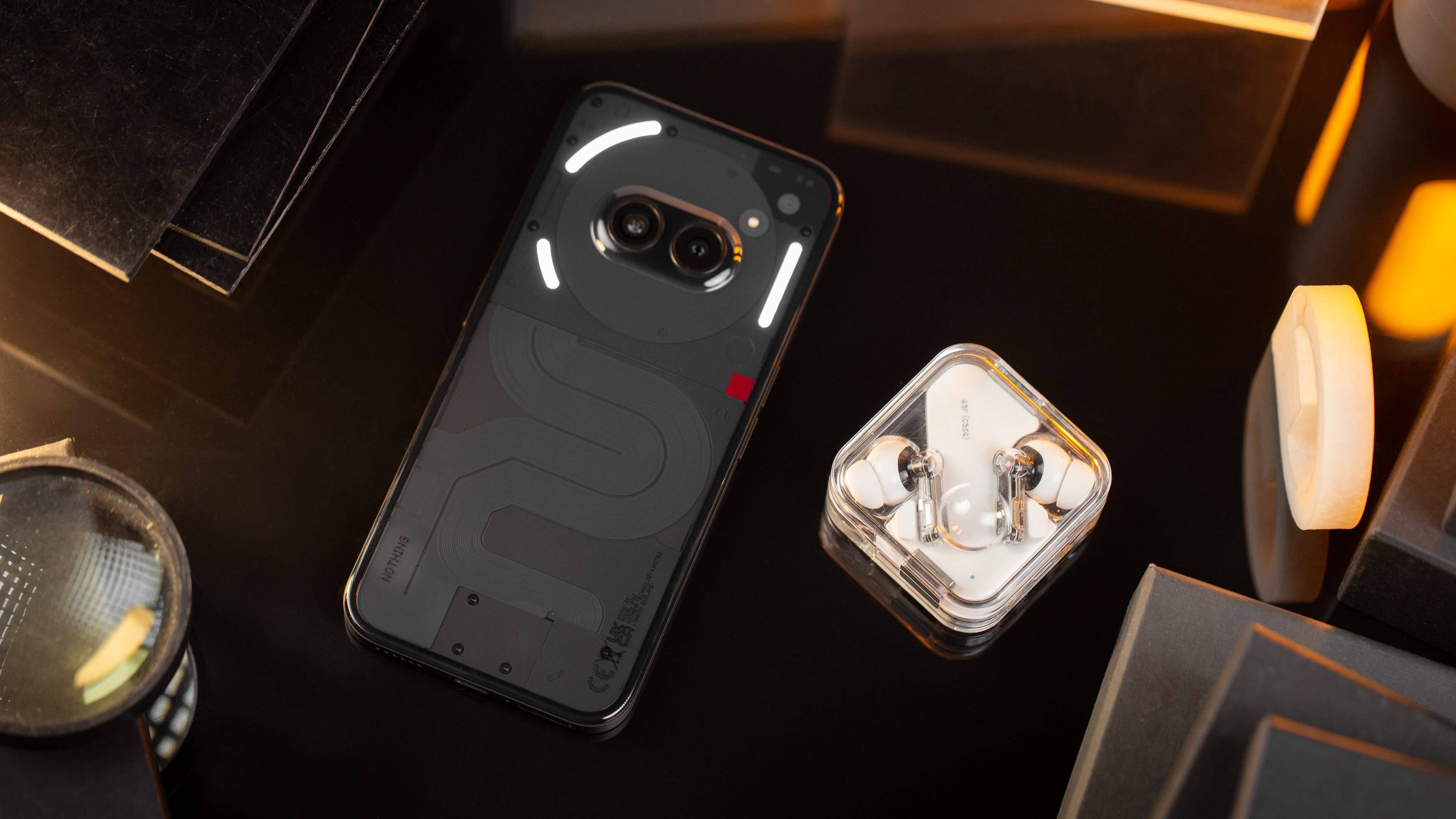 Le Nothing Phone (2a) vu de haut et posé à côté des écouteurs Nothing Ear (2)