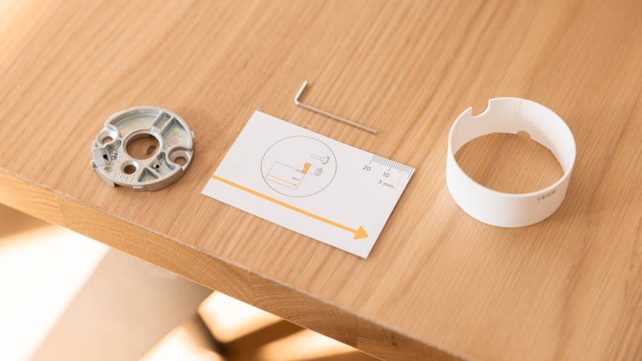 Composants pour Nuki Smart Lock Pro sur une table en bois : une base en métal, un guide du0027installation et un couvercle circulaire.